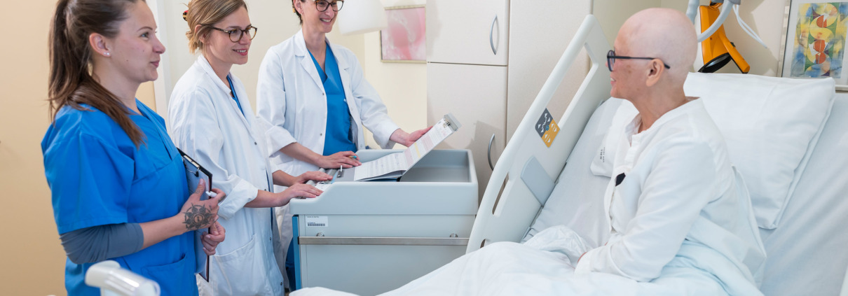 3 Frauen stehen am Bett einer Patientin